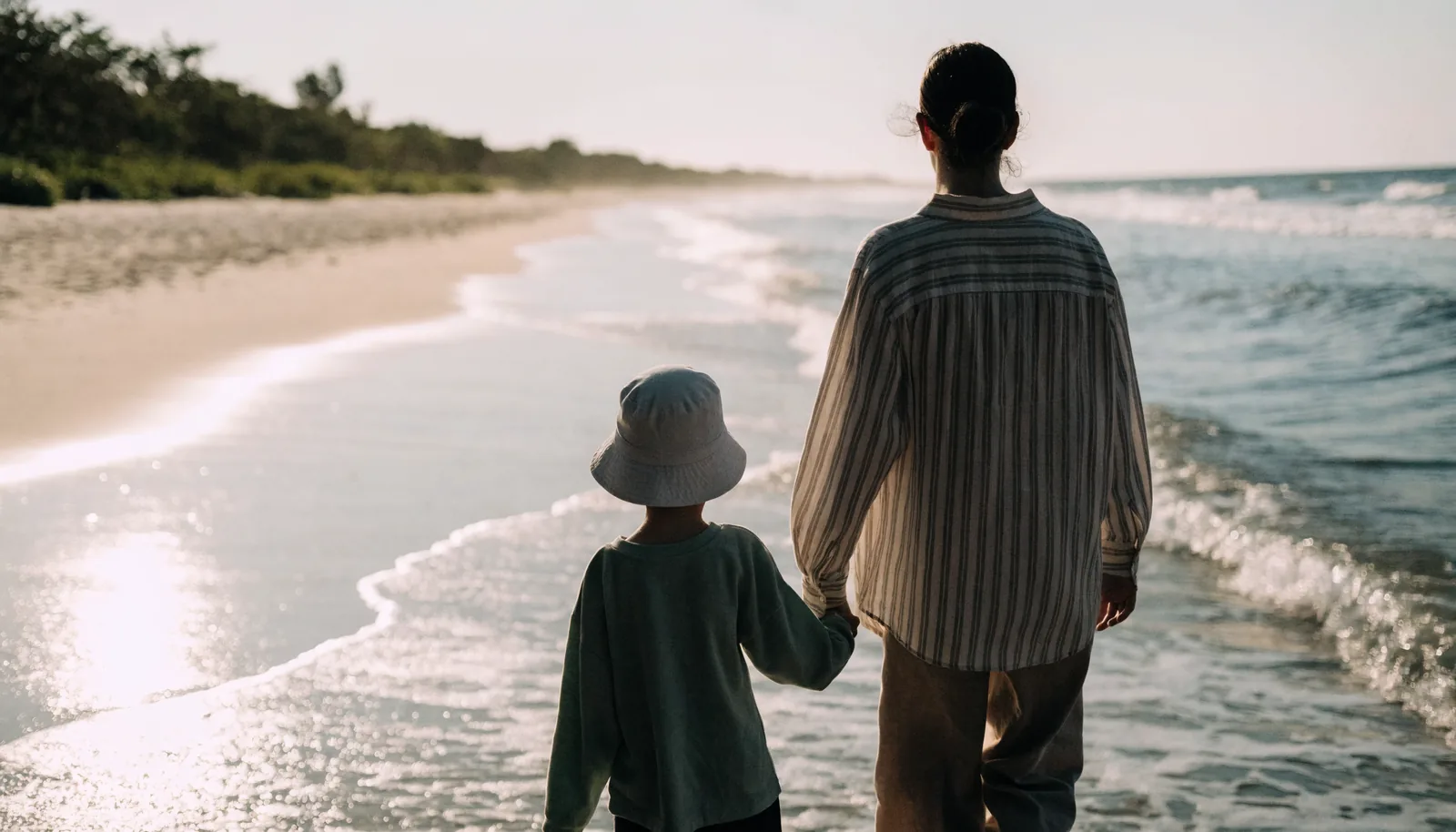 A parent and young child walking hand in hand along the shoreline