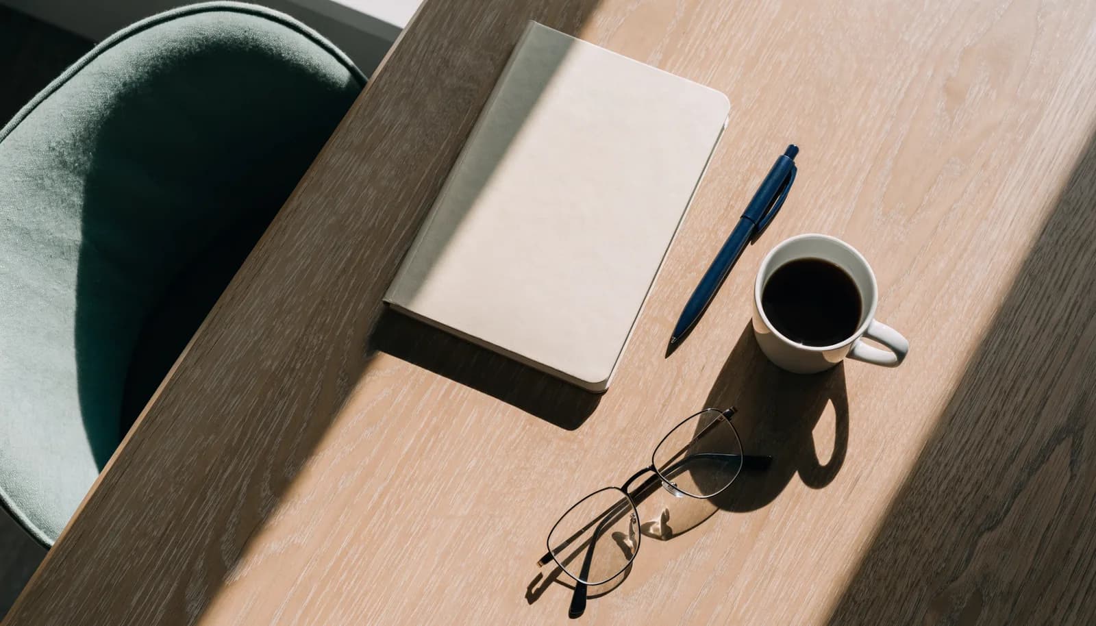 A tidy desk with a notebook, pen, and a cup of coffee in warm light